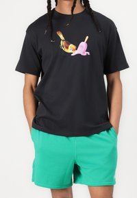 Camiseta negra de manga corta con un gráfico colorido de un pájaro y un polo de fresa. Combinada con unos pantalones cortos de un verde brillante.