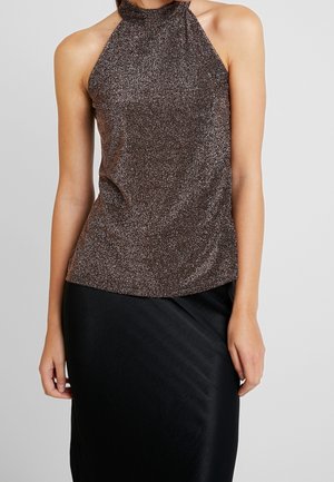 Kobieta ubrana w bezrękawnik z wysokim kołnierzem błyszczący brązowy top i czarną spódnicę, widoczna od ramion do połowy uda na jednolitym tle.