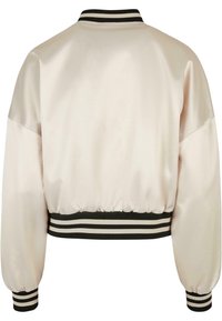 Blouson aviateur en satin couleur crème avec poignets, col et ceinture côtelés à rayures noires et blanches, vu de dos.