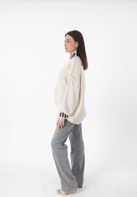 Suéter crema de gran tamaño con un cuello a rayas en blanco y negro, combinado con jeans anchos grises. Tejido de punto ligero, corte relajado.
