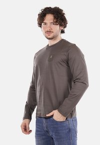 Koszula z długim rękawem w kolorze oliwkowym, wykonana z miękkiego materiału, z kieszenią na piersi z detalem w postaci logo, połączona z niebieskimi dżinsami.