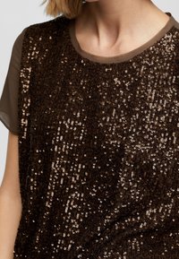 Top marrone con paillettes, caratterizzato da un collo rotondo, maniche corte trasparenti e una superficie texture con paillettes metalliche disposte vicine tra loro.