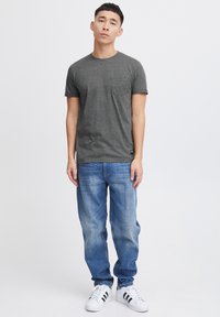 Grå t-shirt med korte ærmer og lomme, stylet med lyseblå denim jeans og hvide sneakers med sorte striber.