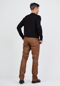 Braune Lederhose mit tailliertem Design, ausgestattet mit zwei Gesäßtaschen und einer glatten Oberfläche. Getragen mit einem schwarzen Langarmshirt.