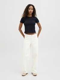 T-shirt de algodão preto com mangas curtas, combinada com calças brancas de perna larga. As calças têm bolsos frontais e fecho de botão frontal.