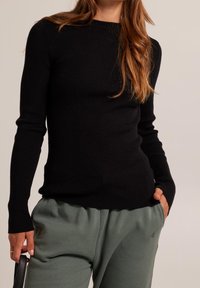 Svart ribbad långärmad tröja med rund halsringning. Matchad med löst sittande gröna sweatpants som betonar avslappnad komfort.