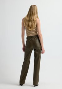 Ärmelloses, beiges Rippoberteil kombiniert mit hochgeschnittenen, olivgrünen Kunstlederhosen, die über Rückentaschen und eine gerade Beinführung verfügen.
