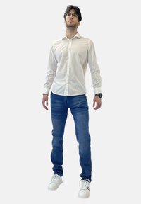 Camisa blanca de botones, jeans azules y zapatillas blancas. La camisa es de manga larga y suave; los jeans son ajustados con una textura de denim clásica.