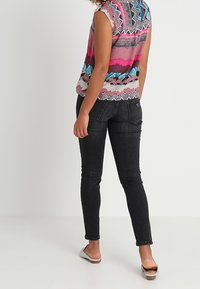 Top sin mangas multicolor con patrones geométricos, combinado con jeans ajustados de mezclilla oscuros y sandalias claras. El conjunto presenta un corte relajado.