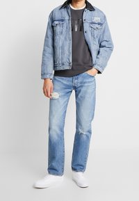 Ljust blå denimjacka med mörk krage, grafisk mörk sweatshirt, ljusblå slitna jeans och vita sneakers. Avslappnad passform.