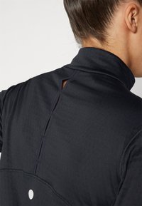 Top sportivo nero con colletto alto e un piccolo taglio sul retro, caratterizzato da una texture liscia e dettagli di cucitura sottili.