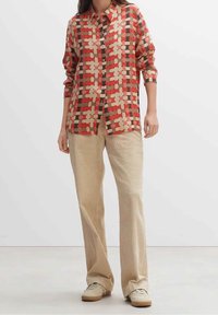 Camicia a motivo intrecciato rosso e beige con colletto, abbinata a pantaloni a gamba larga in corduroy beige e sneakers beige.