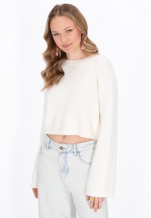Pull court blanc à manches larges, fabriqué dans un matériau tricoté doux. Associé à un jean taille haute bleu clair.
