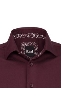 Burgunderfarbendes Hemd mit durchgehender Knopfleiste, das eine floral gemusterte Fütterung im Kragen und ein schwarzes Etikett mit "Kauf"-Branding aufweist.
