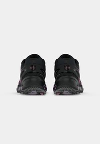 Black athletic shoes with a rounded toe, purple accents, mesh panels, and rubber soles featuring textured grips and a low-profile design.