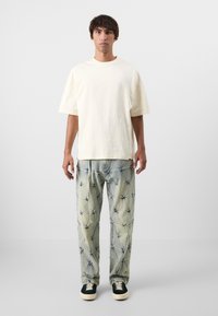 Crème katoenen t-shirt met korte mouwen, gecombineerd met lichtblauwe broek met een sterpatroon en zwarte sneakers met witte zolen.