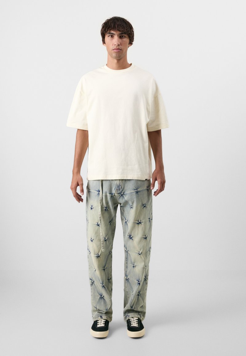 Crème katoenen t-shirt met korte mouwen, gecombineerd met lichtblauwe broek met een sterpatroon en zwarte sneakers met witte zolen.
