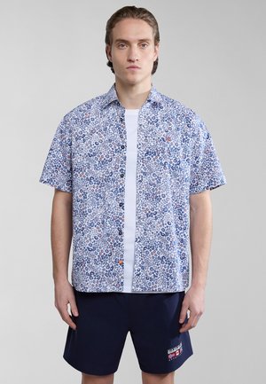 Chemise à manches courtes à boutons de couleur blanche avec un imprimé floral bleu, présentant des accents orange et une poche. Assortie à un short bleu marine.