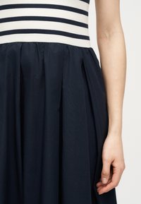 Γυναικείο σώμα που φοράει αμάνικο φόρεμα με λευκό και μαύρο ριγέ πάνω μέρος και φούστα ναυτικού μπλε με πιέτες στη μέση.