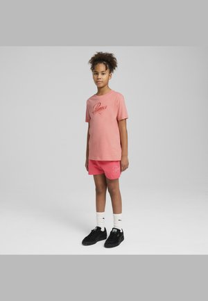Camiseta de algodón rosa con el logo de "Puma" y pantalones cortos rosa a juego. Zapatillas negras con acentos blancos y calcetines de tobillo con estampado.