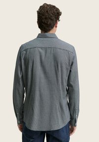Camisa de manga larga a cuadros en tonos grises y negros. Presenta un cuello clásico, puños de botón y dobladillo curvado. Tejido texturizado.