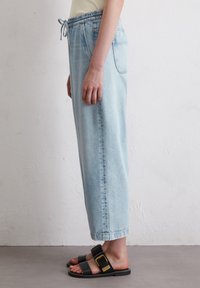 Light blue denim pants with an elastic waistband, side pockets, and a relaxed fit. Paired with black sandals featuring a buckle accent.