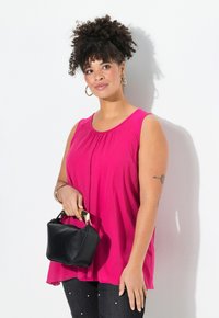 Top sin mangas de color fucsia con escote redondo, combinado con unos jeans oscuros de cintura alta adornados con detalles de perlas, y un pequeño bolso negro.