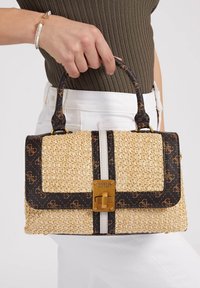 Sac à main en paille tissée avec un logo foncé, des éléments métalliques dorés et une forme structurée présentant une bande blanche contrastante au centre.