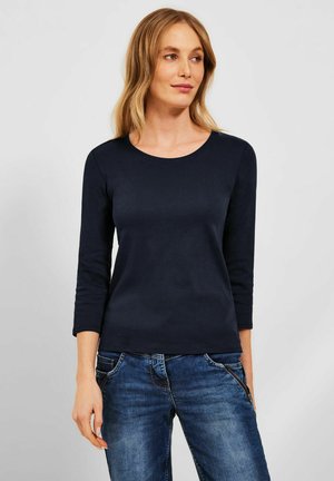Marinblus med lång ärm och rund halsringning, tillverkad av slät tyg. Matchad med blå jeans med framfickor och en avslappnad passform.