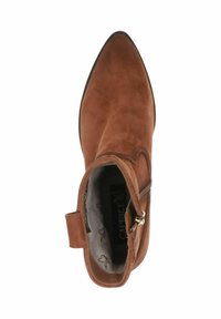 Stivale alla caviglia in suede marrone con punta affusolata, cerniera laterale e un anello per facilità di indossatura. Fodera interna morbida con un motivo ripetitivo.