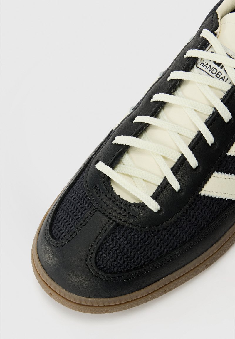 Sneaker en cuir noir et textile tissé avec des lacets blancs, présentant une surface texturée et une semelle en caoutchouc. Logo sur la languette.