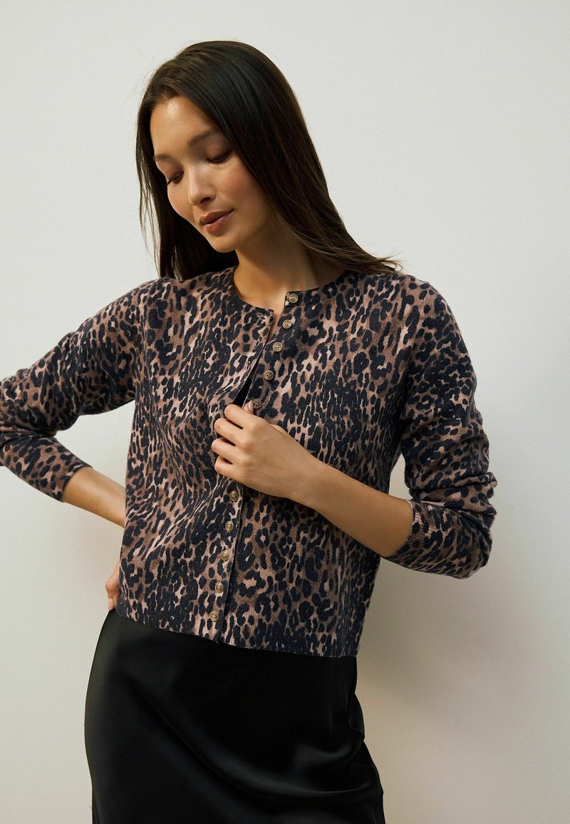 Cardigan imprimé léopard en tissu doux, avec un col rond et des boutons dorés sur le devant. Manches longues avec des poignets ajustés.