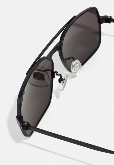 Occhiali da sole neri con un design geometrico, lenti scure e dettagli in metallo. Presentano naselli in gomma e bracci sottili. Fascette delle tempie testurizzate.