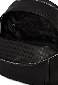 El interior de la mochila negra de cuero presenta un forro de tela texturizada con un patrón sutil, un bolsillo con cremallera y bordes suaves para una mejor organización.