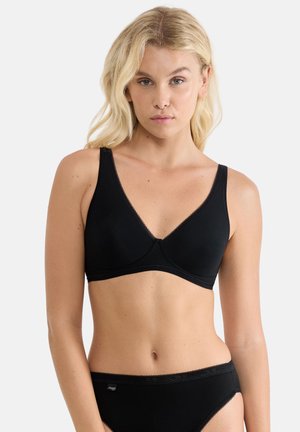 Blonde woman wearing a black soft cup bra and matching black briefs, standing against a plain light background.