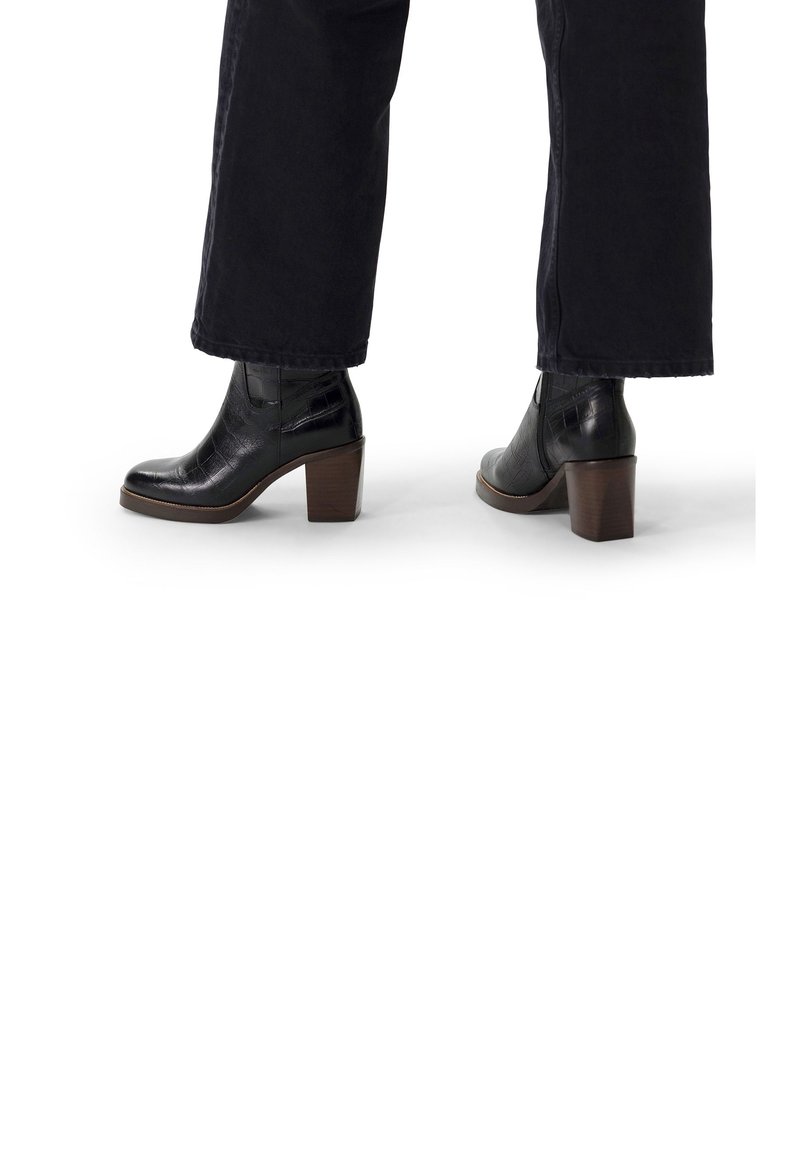 Stivaletti neri in pelle con finitura testurizzata, punta quadrata e tacco spesso marrone. Indossati con pantaloni scuri, visibile la vista laterale.