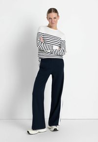 Lange marineblaue Hosen mit weißen Seitennähten, kombiniert mit einem langärmligen Oberteil mit weißen und marineblauen Streifen. Glattes Material und lockere Passform.