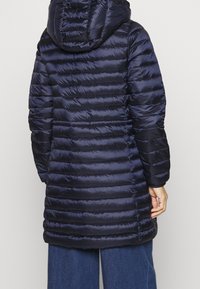 Laivastonsininen toppatakki, tikattu malli, istuva huppu, pitkät hihat, sileä pinta ja suora helma. Ei näkyviä kiinnityksiä tai koristeluja.