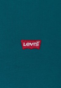 Tessuto lavorato a maglia color verde acqua con una vistosa toppa del logo Levi's ricamata in rosso, a forma di rettangolo curvo.