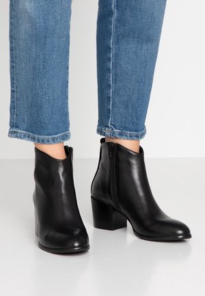Bottes cheville en cuir noir à bout arrondi, fermeture éclair latérale et talon bloc, associées à un jean en denim bleu raccourci.