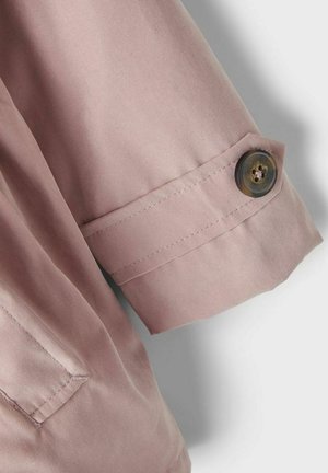 Poignet de chemise rose clair avec fermeture à bouton. Le tissu est doux, lisse et présente des coutures soignées. Le bouton est foncé avec un effet marbré.
