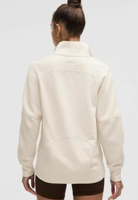 Sweatshirt texturat de culoare bej deschis, cu guler înalt, umeri lăsați și logo pe spate. Design simplu, cu o siluetă relaxată.