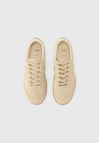 Sneakers beige in suede con lacci piatti, suole in gomma e dettagli di cucitura sottili. L'interno presenta il branding dorato "BOSS" su una soletta beige.