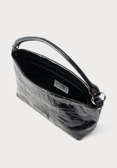 Μαύρη τσάντα από δερματίνη με υφή, με μία λαβή και εμφανή εσωτερική τσέπη με φερμουάρ, πάνω σε απλό φωτεινό φόντο.