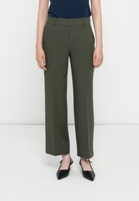 Pantalones de traje verde oliva con un diseño de frente plano y pierna ancha, y lazos para cinturón. Combinados con bailarinas negras de punta.
