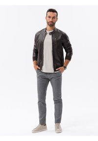 Giacca bomber in pelle nera, t-shirt grigia chiara, pantaloni grigi e sneakers beige. Le caratteristiche includono dettagli con cerniera e polsini a costine.