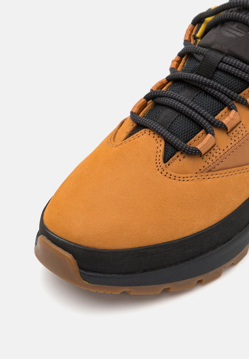 Pomarańczowa skórzana cholewka z czarną siateczką i detalami w postaci sznurówek, gumowa podeszwa z teksturowanym gripem, zaokrąglony nosek oraz jednolite wzory przeszycia.