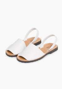 Valged slingback sandaalid avatud varbaosaga, lame pruun tald ja valged õmblused; minimalistliku stiili ja pehme tekstuuriga disain.