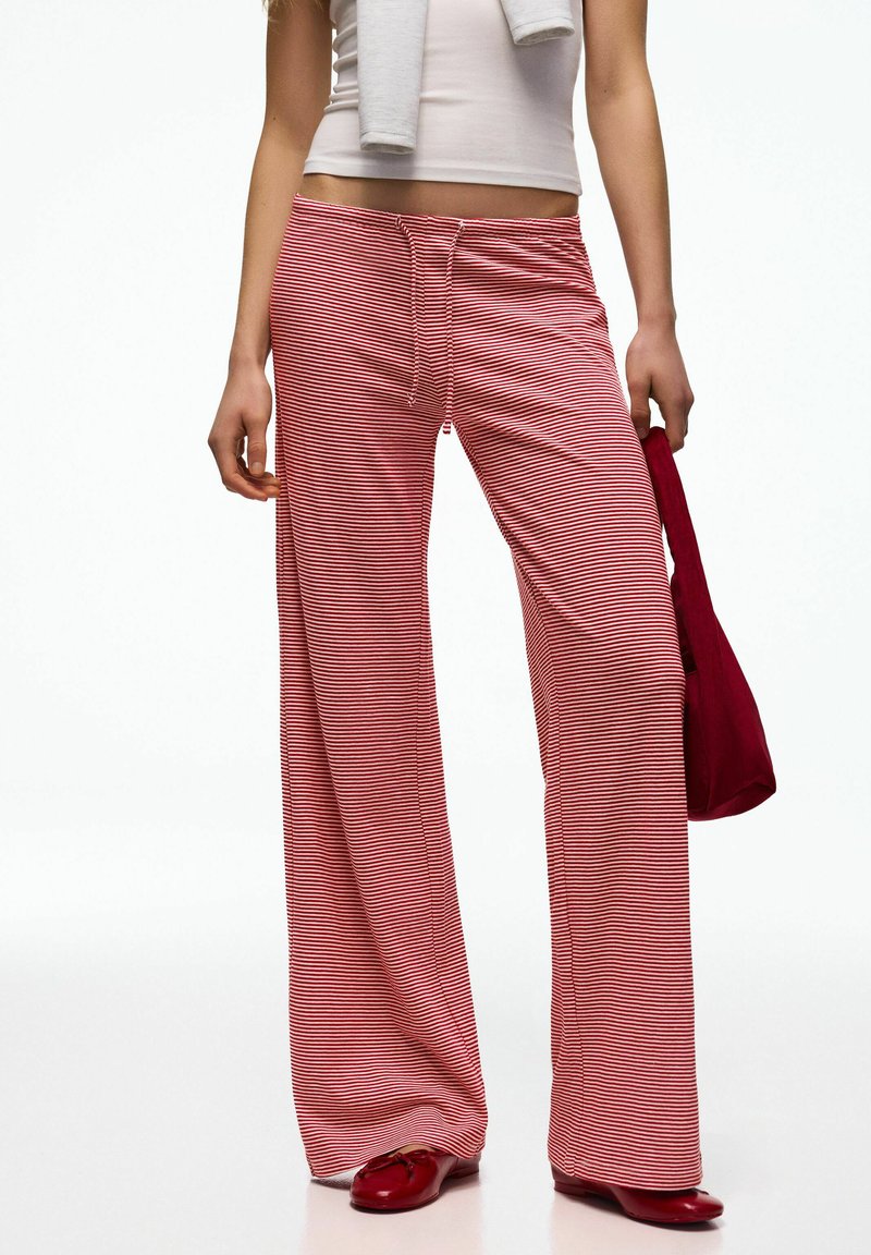 Femme portant un pantalon large à rayures étroites rouges et blanches, un haut court blanc, tenant un sac rouge et portant des chaussures rouges.