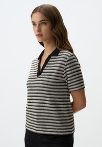 Polo shirt a maniche corte a righe bianche e nere con scollatura a V profonda e colletto nero; tessuto a maglia testurizzato con dettagli argentati.